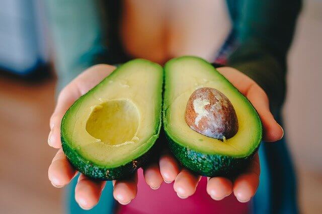 mujer sosteniendo aguacate en rodajas